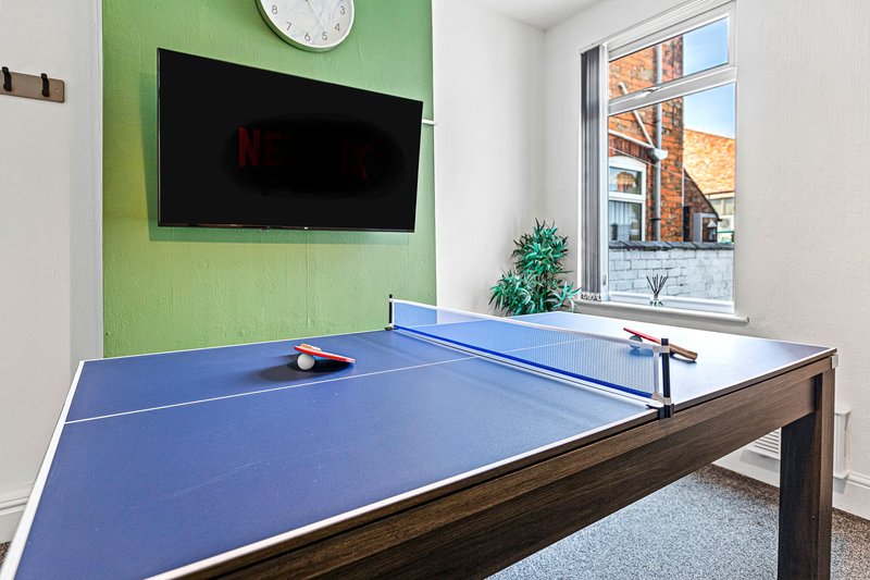 Games room with blue ping pong table, wall-mounted TV, green accent wall, and window view