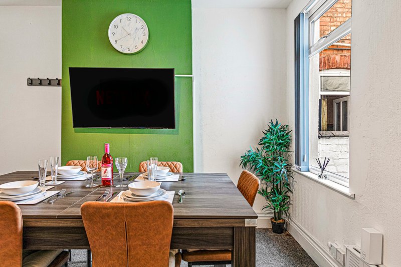 Dining area with wooden table, brown leather chairs, green accent wall and wall-mounted TV