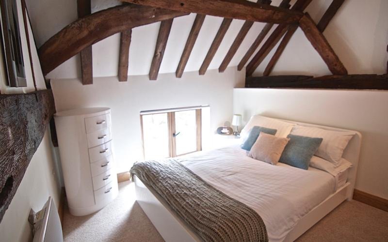 Bright attic bedroom with exposed timber beams, double bed, and chest of drawers