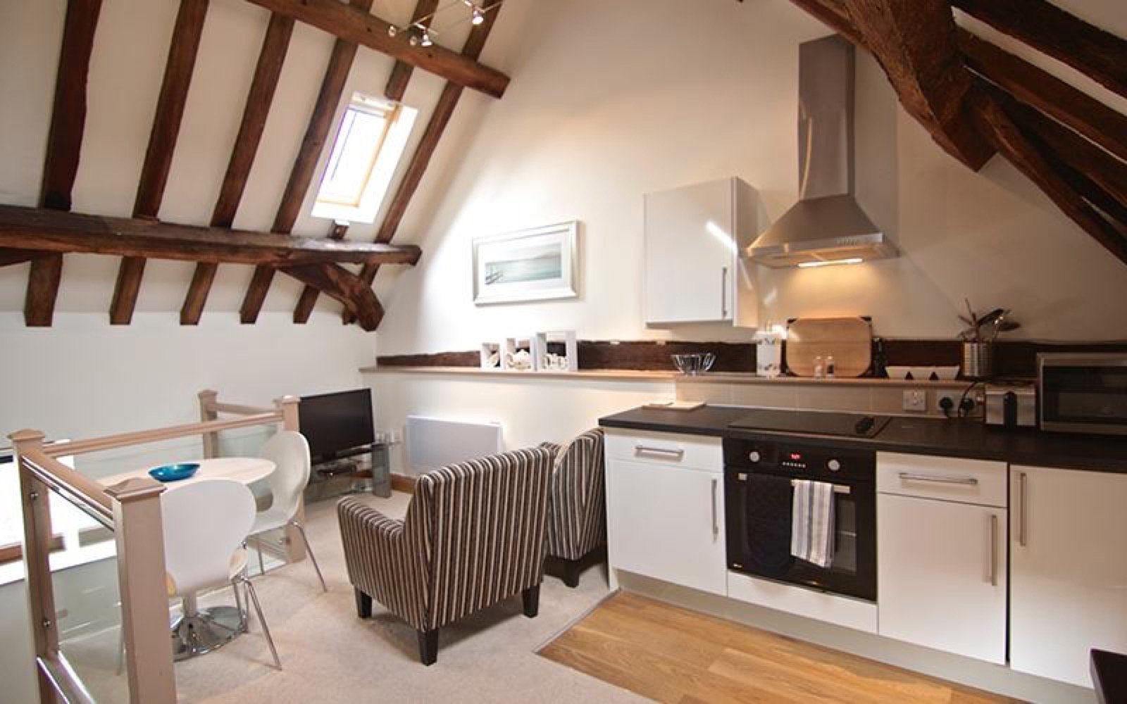 Open-plan kitchen and dining area with exposed beams, white cabinetry, and wooden flooring