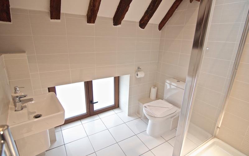 Clean modern bathroom with white tiles, toilet, sink, shower enclosure and window