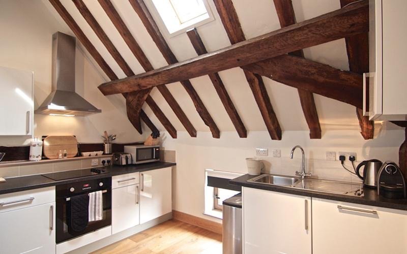 Modern kitchen with exposed wooden beams, white cabinetry, stainless steel appliances and skylight