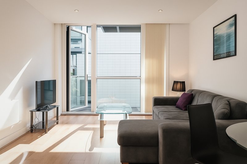 Modern living room with gray sofa, TV stand, floor-to-ceiling windows and wooden flooring
