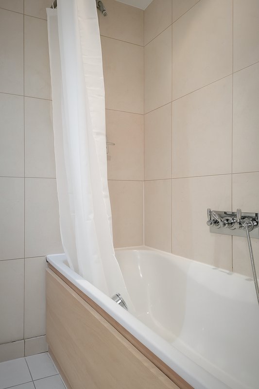 Bathroom with white bathtub, shower curtain rod, and cream-coloured tile walls