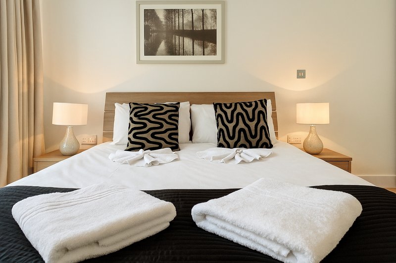 Modern bedroom with double bed, patterned cushions, folded towels and bedside lamps