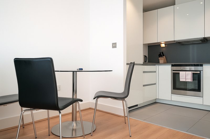 Modern open-plan kitchen and dining area with white cabinetry, black dining chairs, and wooden flooring