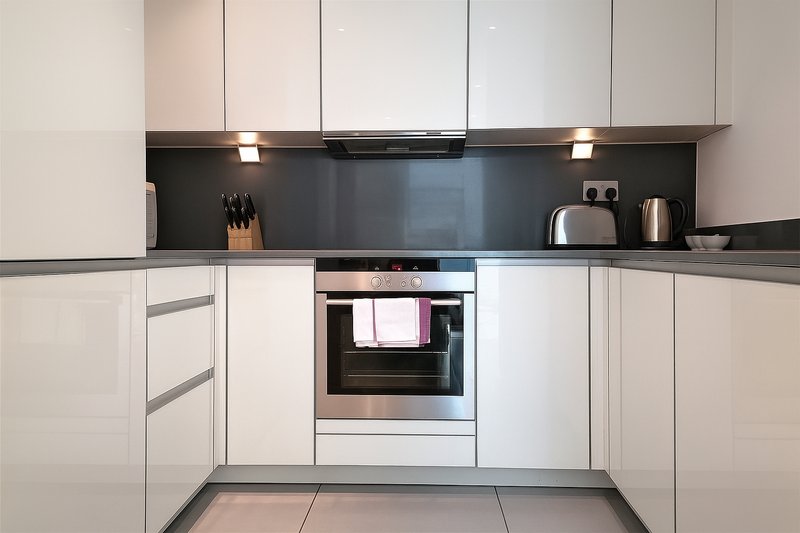 Modern white kitchen with built-in oven, black backsplash, stainless steel appliances and gray flooring