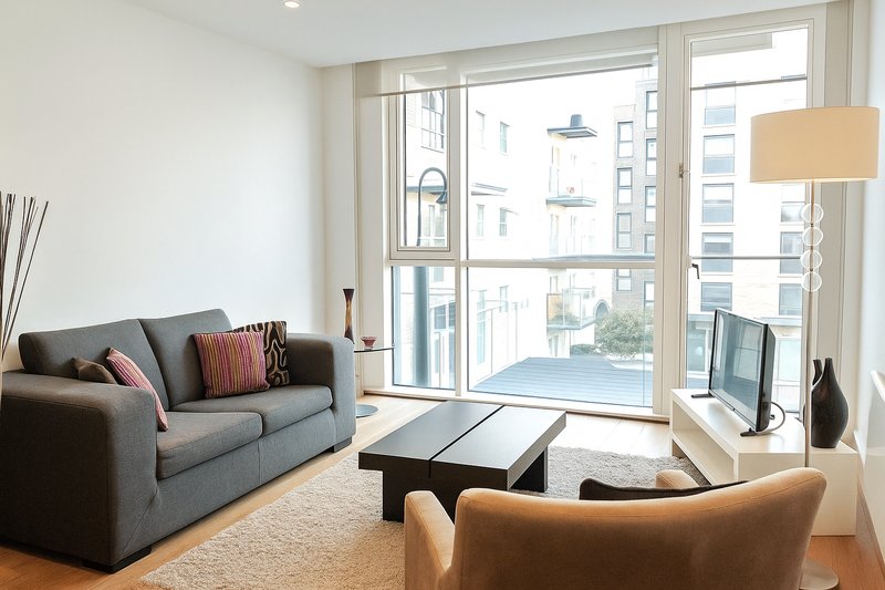 Modern living room with gray sofa, tan armchair, coffee table and balcony doors overlooking city