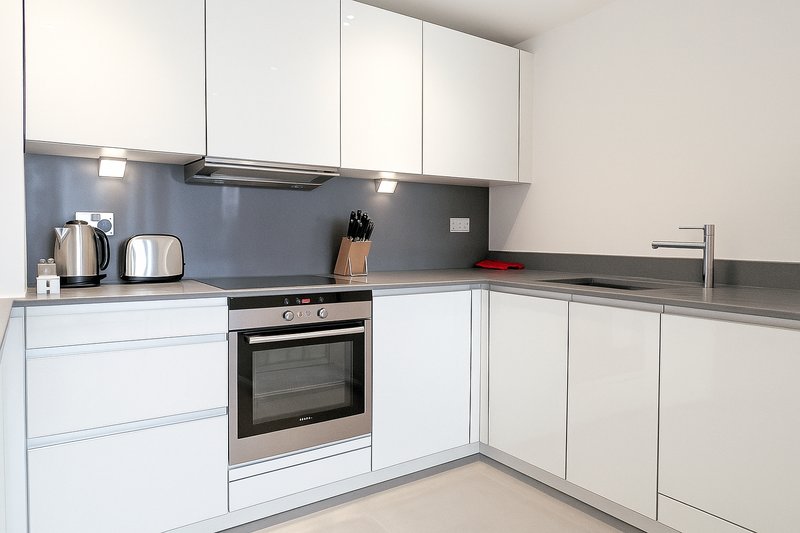 Modern white kitchen with built-in oven, blue backsplash, stainless steel appliances and granite countertop