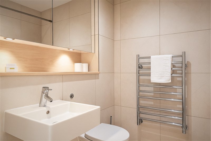 Modern bathroom with white sink, toilet, heated towel rail and illuminated mirror cabinet
