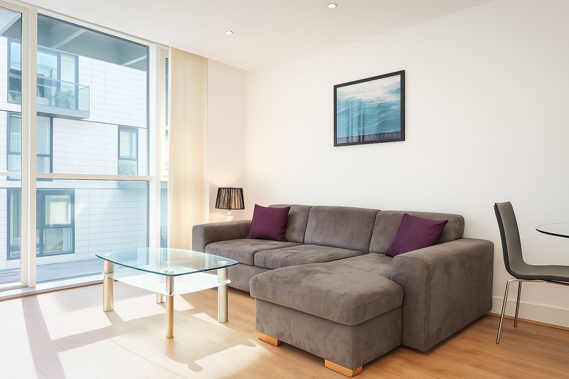 Modern living room with gray sectional sofa, glass coffee table, and large windows overlooking cityscape