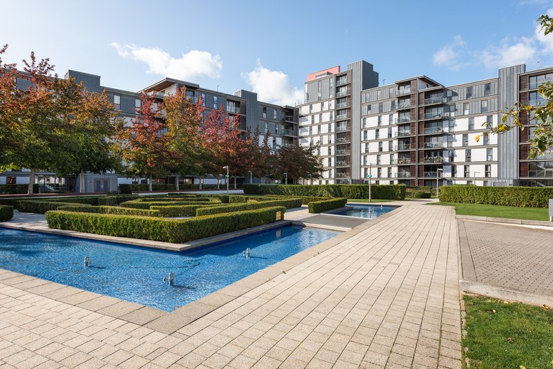 Modern apartment complex exterior with swimming pool, wooden deck, landscaping and multiple residential buildings