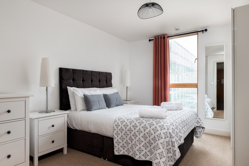 Bright modern bedroom with black upholstered bed, white nightstands, and burgundy curtains