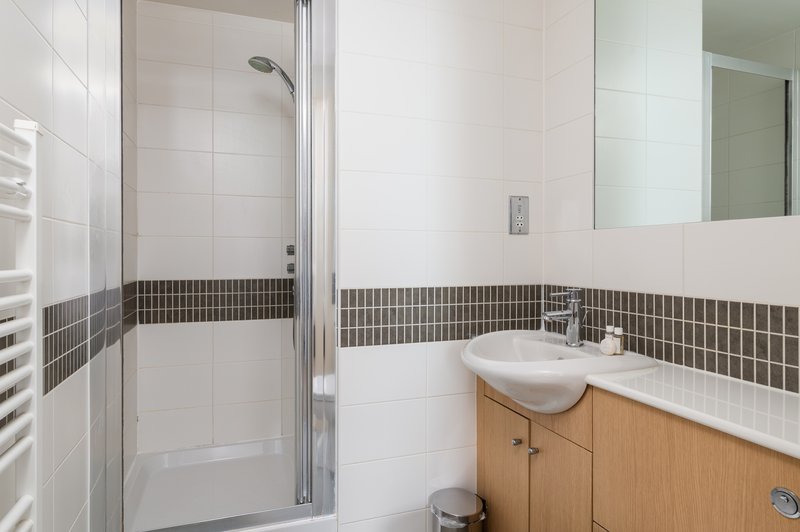Modern bathroom with walk-in shower, white tiles, dark stripe accent, wooden vanity and mirror
