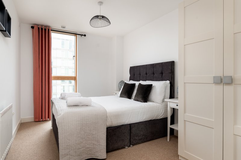 Bedroom with double bed, black headboard, white bedding, red curtains, and built-in wardrobe