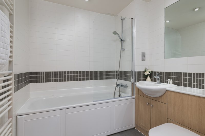 Modern bathroom with white subway tiles, dark accent stripe, bathtub with glass panel, wooden vanity and mirror