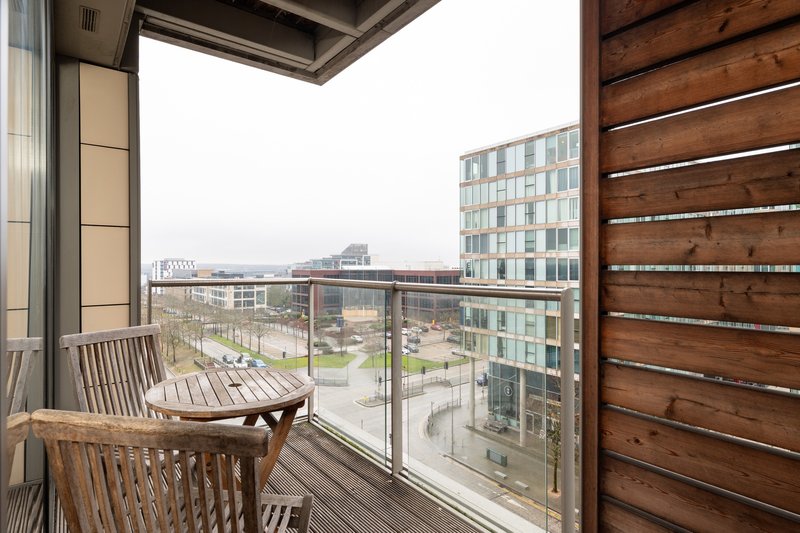 Modern apartment balcony with wooden chairs overlooking urban courtyard and buildings
