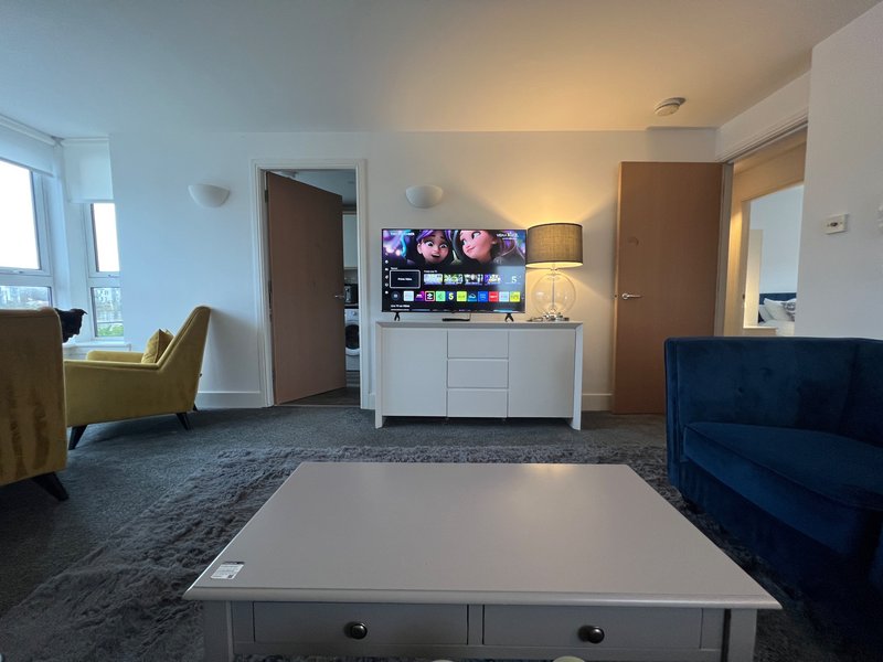 Modern living room with white coffee table, blue sofa, wall-mounted TV, and armchair