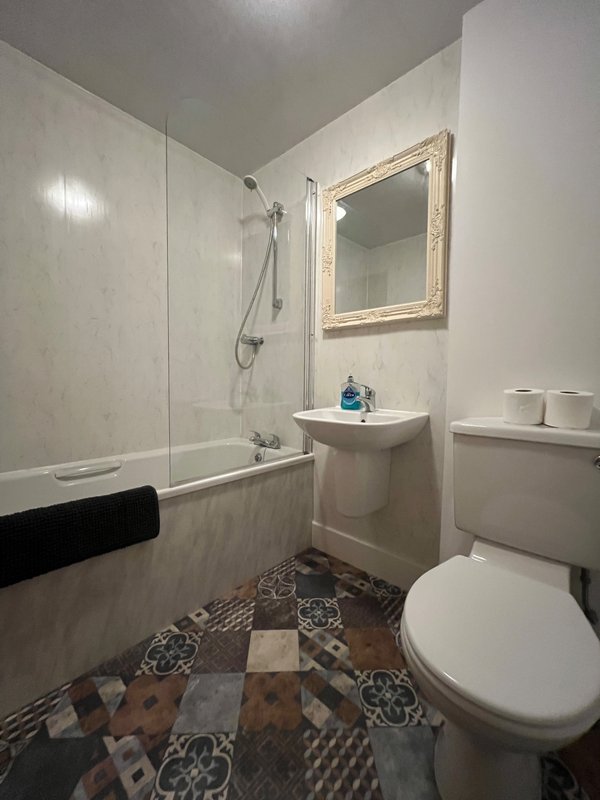 Bathroom with toilet, pedestal sink, mirror, shower enclosure and patterned floor tiles