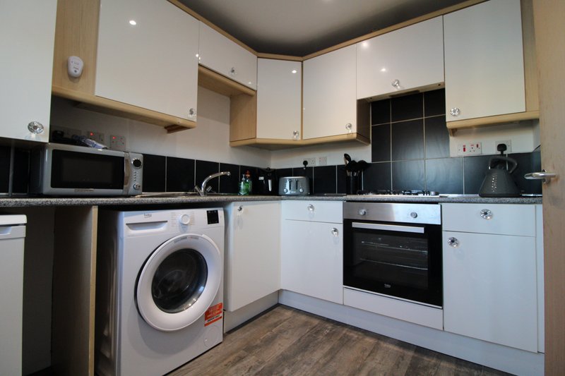 Modern kitchen with white and wood cabinetry, black tile backsplash, integrated appliances and washing machine
