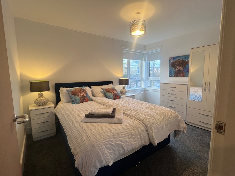 Bright modern bedroom with double bed, white bedding, black headboard, twin nightstands with lamps