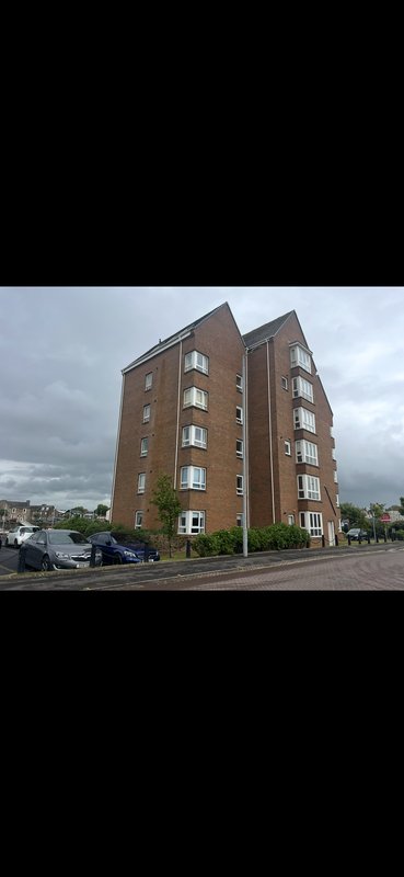 Brick apartment building with multiple floors, windows, and street parking visible