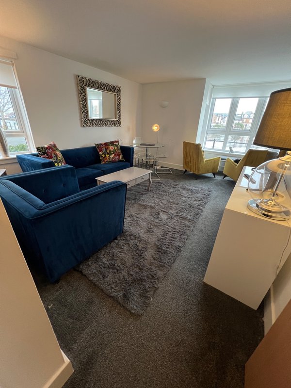 Modern living room with blue sectional sofa, gray area rug, and large windows overlooking cityscape
