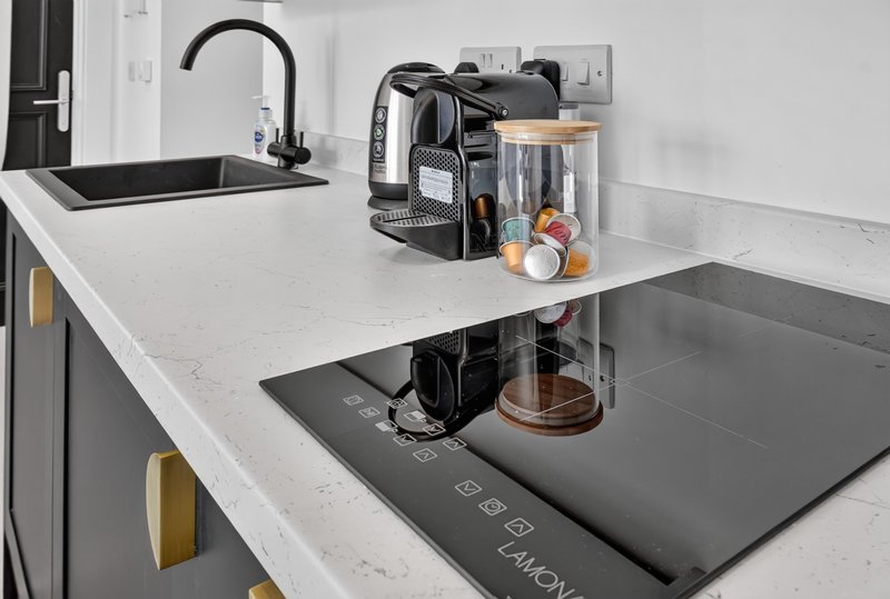 Modern kitchen counter with black tap, coffee machine, kettle and induction cooktop