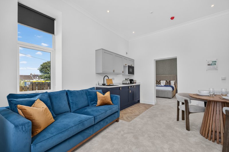 Open-plan living area with blue sofa, kitchenette, dining table and large window with garden view