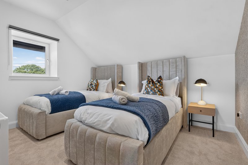 Bright twin bedroom with two upholstered beds, blue bedding, wooden nightstand, and window with garden view