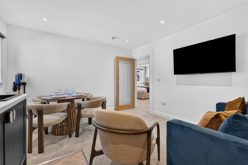 Modern open-plan living area with dining table, sofa, wall-mounted TV and kitchen