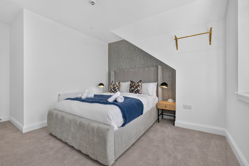 Modern bedroom with grey upholstered bed, white bedding, navy throw, and brass wall-mounted rail