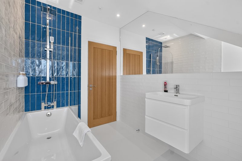 Modern bathroom with bathtub, blue tile feature wall, white vanity and wooden door