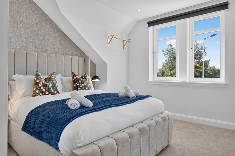 Modern bedroom with upholstered bed, blue throw blanket, large window with garden view