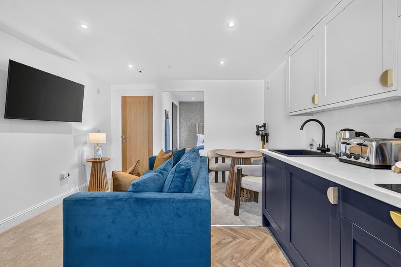 Open-plan living space with blue sofa, kitchen with navy cabinetry, and wall-mounted TV