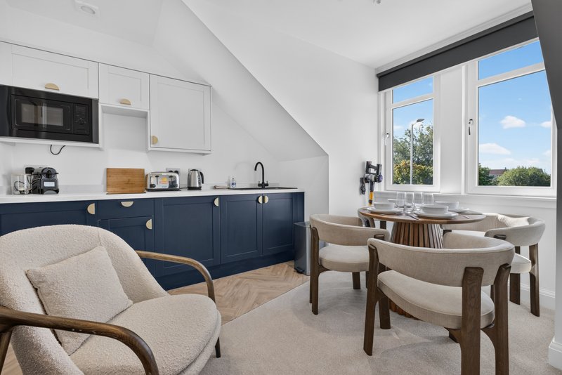 Open-plan kitchen and living area with navy cabinetry, dining table, upholstered chairs and large windows