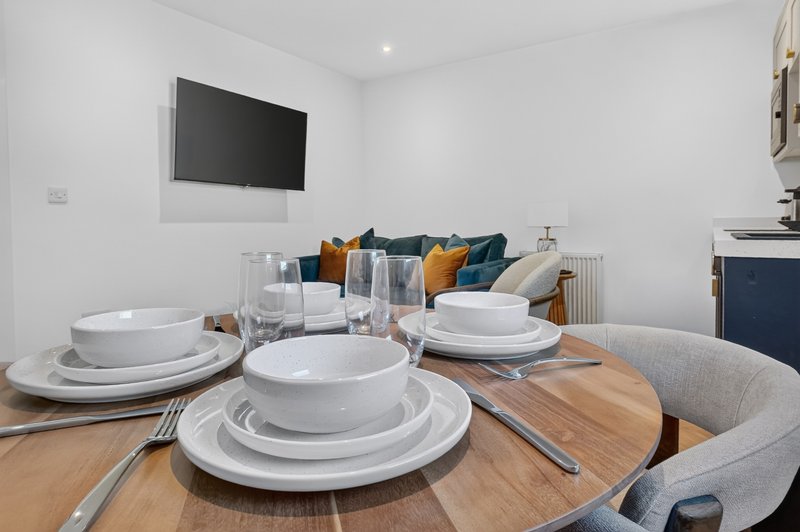 Open-plan dining and living area with round wooden table, place settings, and sofa with cushions