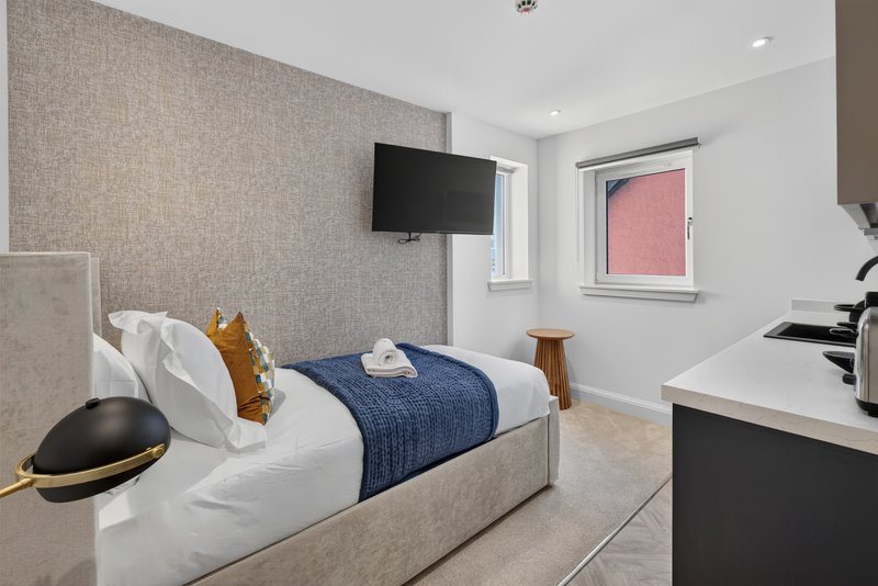 Modern bedroom with single bed, blue throw, wall-mounted TV and desk area