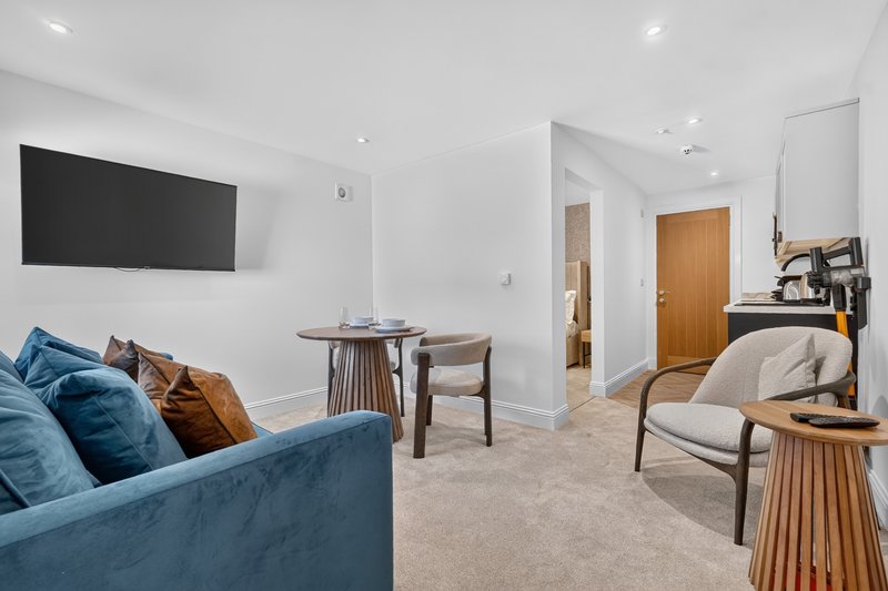 Modern open-plan living area with blue sofa, wall-mounted TV, wooden furniture and cream carpet