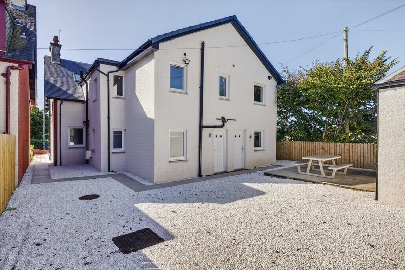 Modern two-story house with cream and purple rendered walls, gravel driveway, and garden seating area