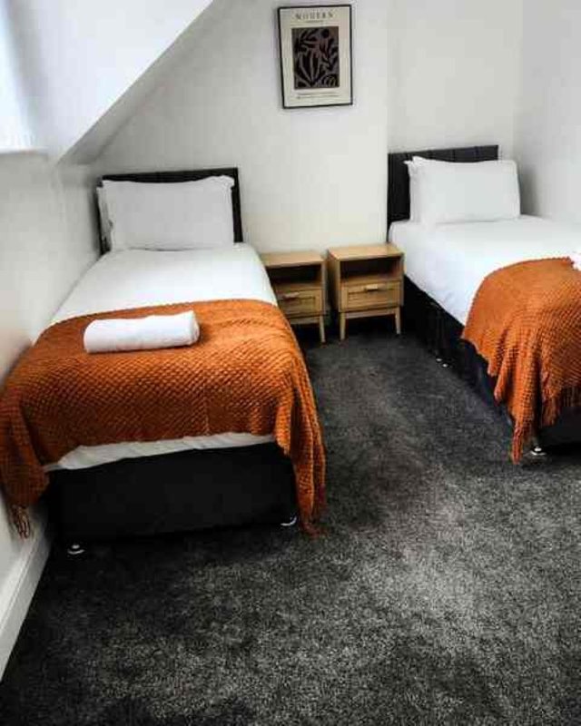 Twin bedroom with two single beds, wooden nightstands, orange throws and white pillows