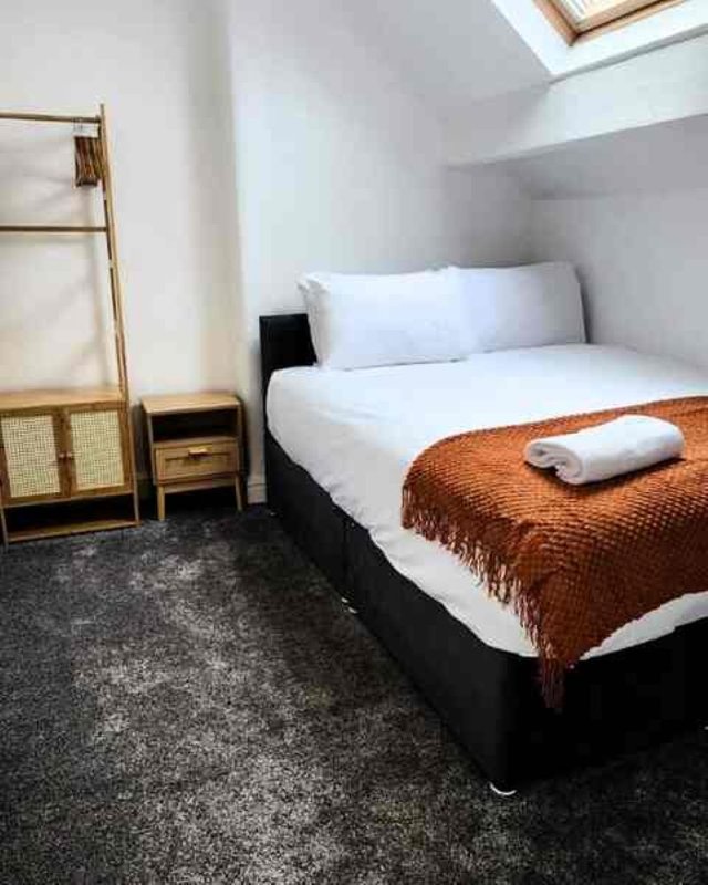 Modern bedroom with double bed, brown throw blanket, white pillows and wooden room divider