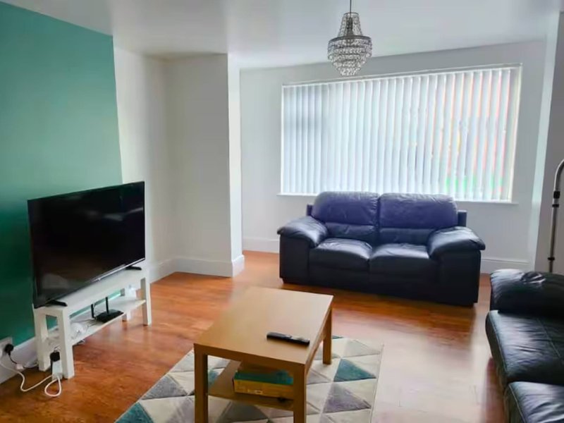 Living room with dark blue sofa, wooden coffee table, TV, and large window with blinds