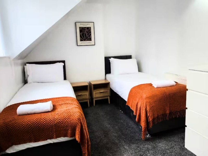 Attic bedroom with two single beds, orange blankets, white pillows and wooden bedside tables