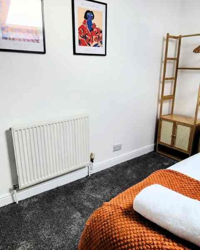 Bedroom with single bed, orange blanket, white pillow, radiator, and wall art