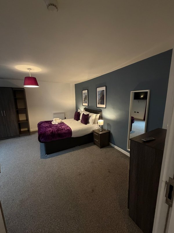 Spacious bedroom with double bed, purple bedding, dark feature wall, and pendant lighting