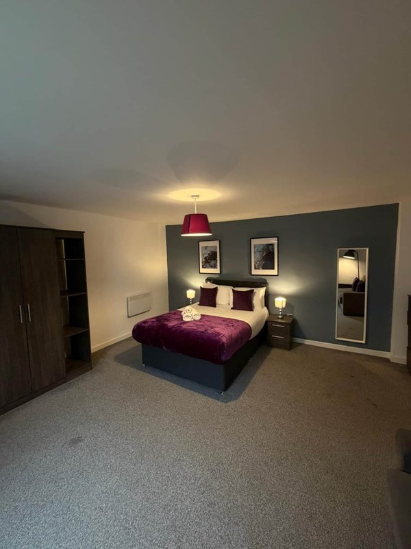 Modern bedroom with purple velvet bed, dark feature wall, bedside lamps and framed artwork