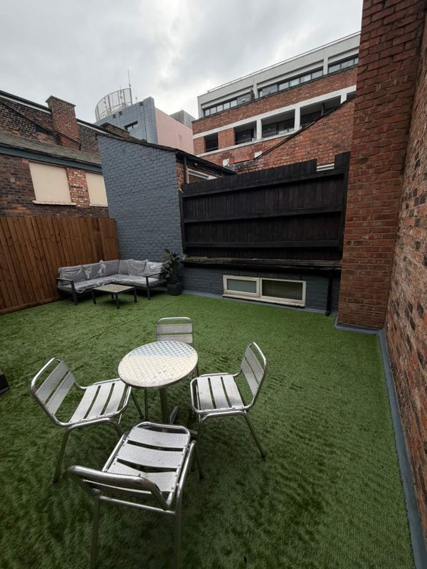 Enclosed courtyard with artificial grass, dining table, chairs and seating area against brick walls