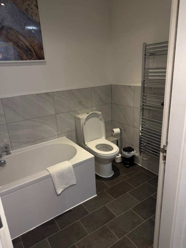 Modern bathroom with white bathtub, toilet, heated towel rail and dark tile flooring