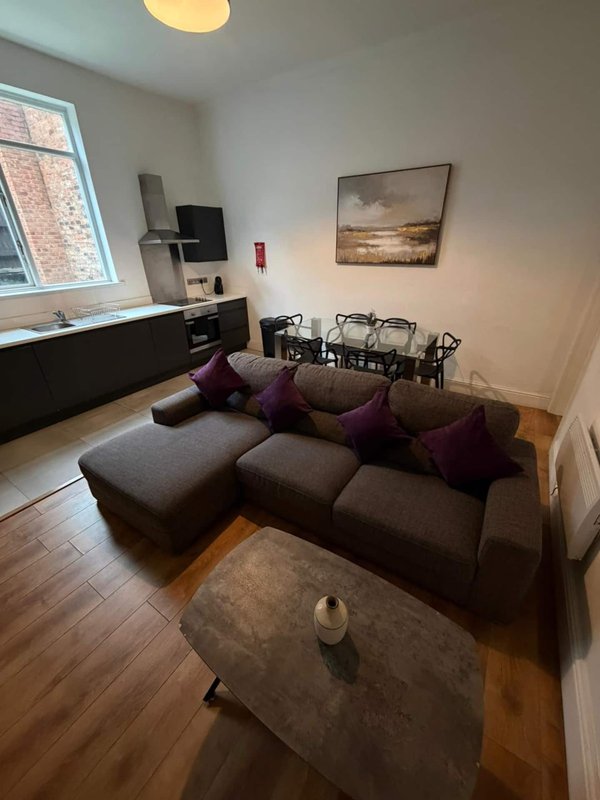 Living room with brown sectional sofa, purple cushions, wooden floor and window